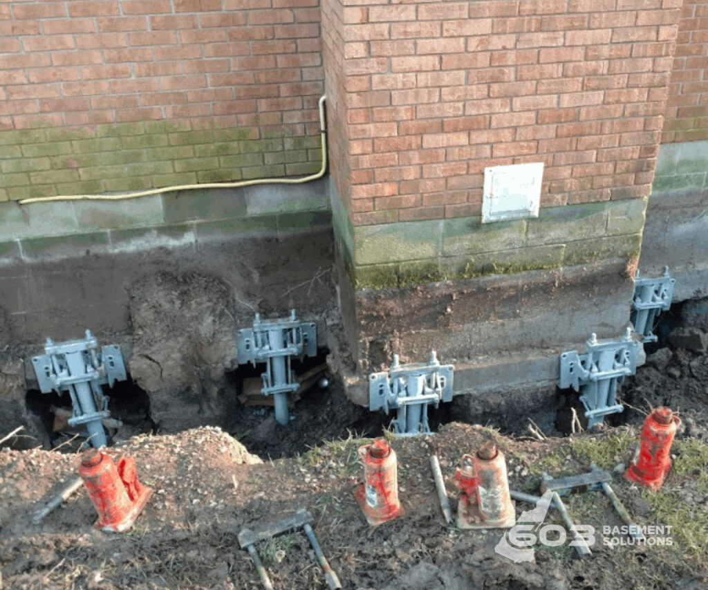 Multiple steel push-pier brackets installed along a brick foundation by 603 Basement Solutions