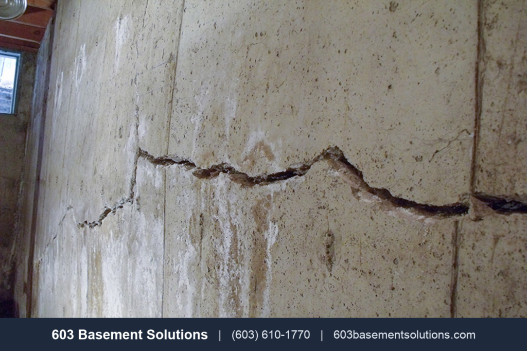 Horizontal crack across a foundation wall with efflorescence, a sign of foundation failure in an older New Hampshire basement