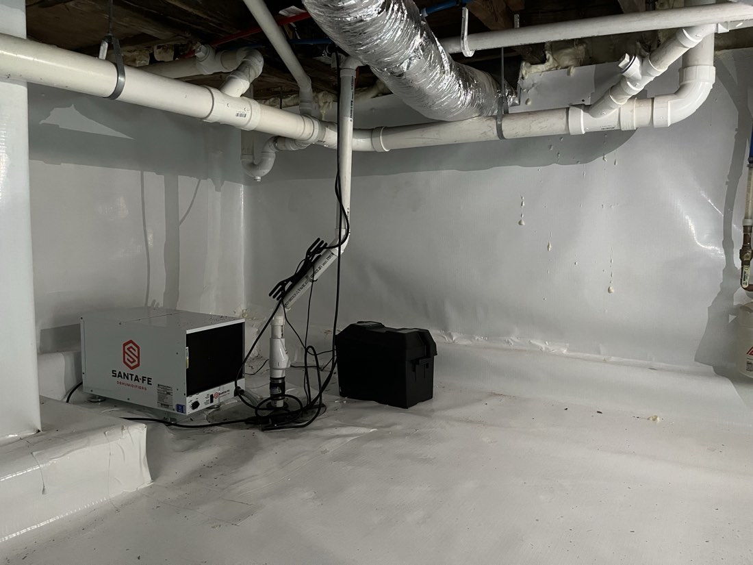 Fully encapsulated crawl space: sealed white liner on floor and walls, taped seams, spray-foamed rim, Santa Fe dehumid