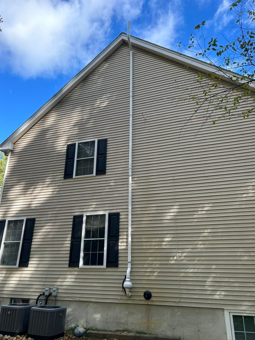 Exterior radon mitigation riser up a tan vinyl gable end, fan at the base, discharge above the roofline.